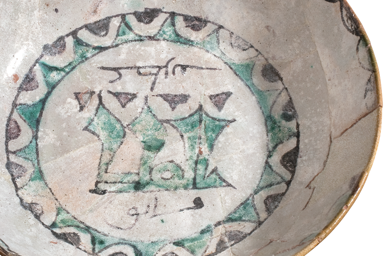 A deep round dish decorated at the center with a ring of geometric forms enclosing calligraphy. Scalloped decoration is painted around the rim.