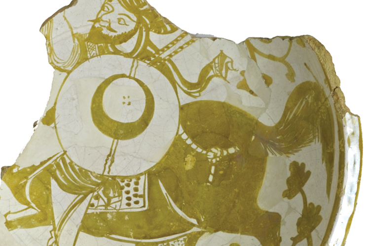 The ceramic fragment of a dish painted at the center to depict a man carrying a shield and riding a horse, along with a rabbit and vegetal designs.