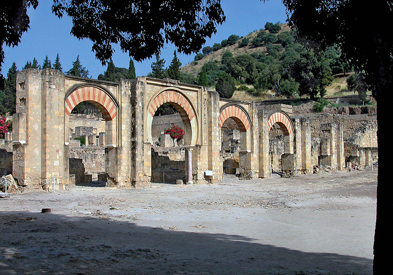 An oblique view of the façade of four horseshoe arches opening onto the ruins of an open plaza.