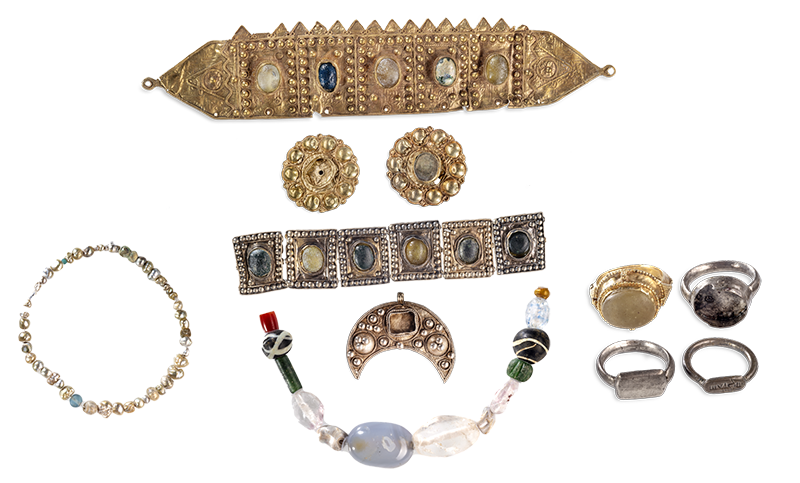 A long gold rectangular band comprising five rectangular panels, each inset with a single translucent stone and decorated with raised dots along the sides and top of each panel. Two circular gold discs decorated with raised dots around the circumference and inset with a translucent stone. A silver rectangular band comprising six square disks, each inset with a single translucent or opaque stone and decorated with raised dots along all four sides of each panel. A string of pearls and glass beads. A crescent-shaped flat gold disk decorated with two large and multiple small, raised dots, and inset with a translucent stone. A string of thirteen translucent and opaque beads. A gold ring with an oval opaque stone. A silver ring with an oval opaque stone. Two silver rings, each with a blank rectangular plaque at the center.