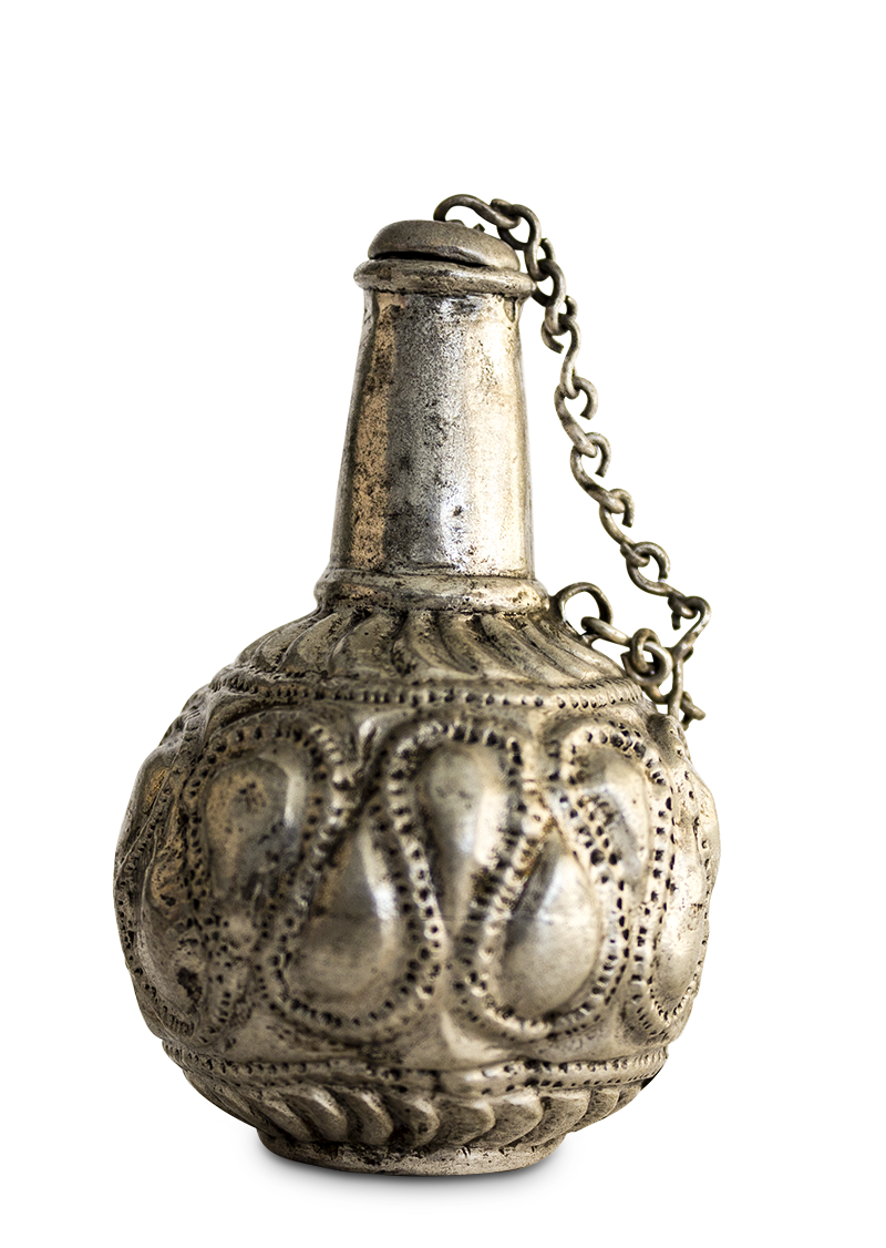 A globular silver vessel decorated in relief with a serpentine design, with a narrow neck and a chain that secures the cap to the bottle.