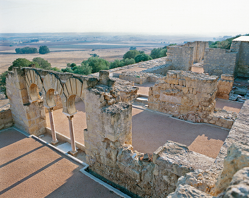 An elevated view of the remains of stone walls including three horseshoe arches.