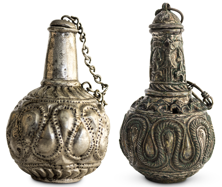 A globular silver vessel decorated in relief with a serpentine design, with a narrow neck and a chain that secures the cap to the bottle.